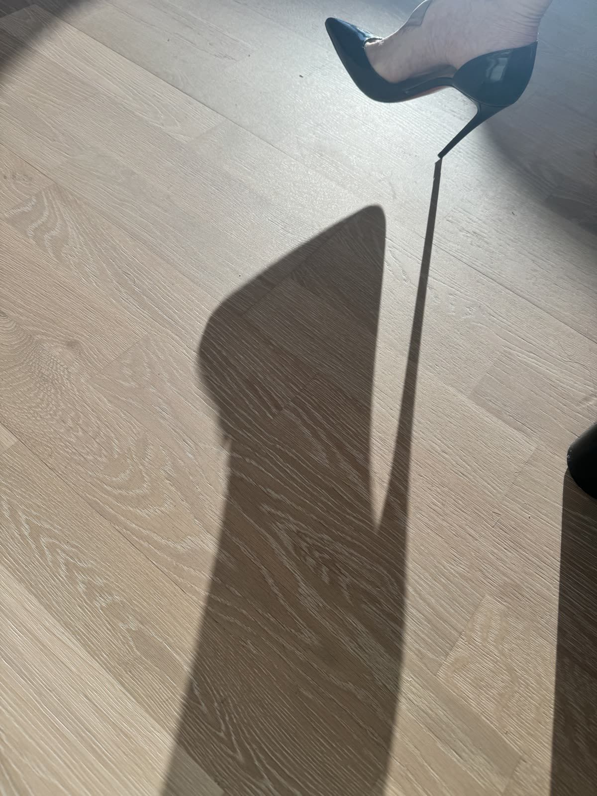 A long shadow cast across a pale floor by Aria in a high heel.